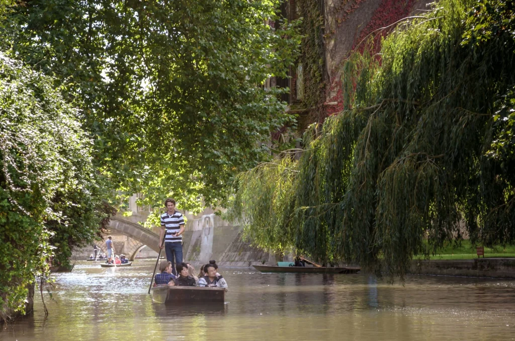 River tour guide standing on punt wearing white and black uniform.